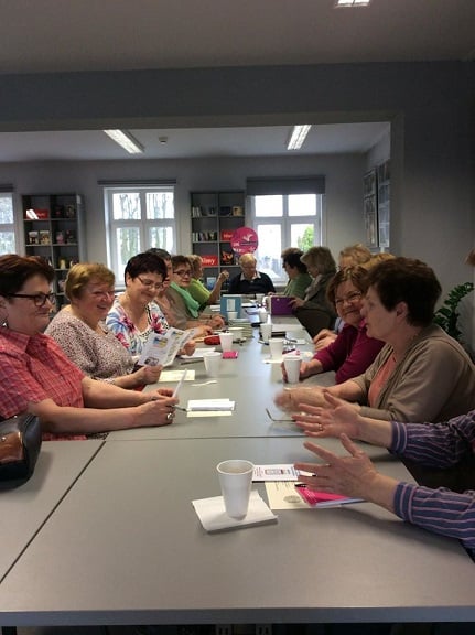 Wnętrze biblioteki,mediateka. Przy stolikach siedzą uczestnicy DKK UTW wspólnie omawiają książkę E.E.Schmitta: "Tajemnica pani Ming".