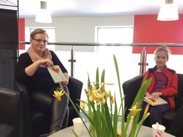 Dwie uczestniczki DKK SP 3 wspólnie omawiają książkę Érica-Emmanuela Schmitta "Oskar i pani Róża". Na stoliku stoją żółte kwiaty. 