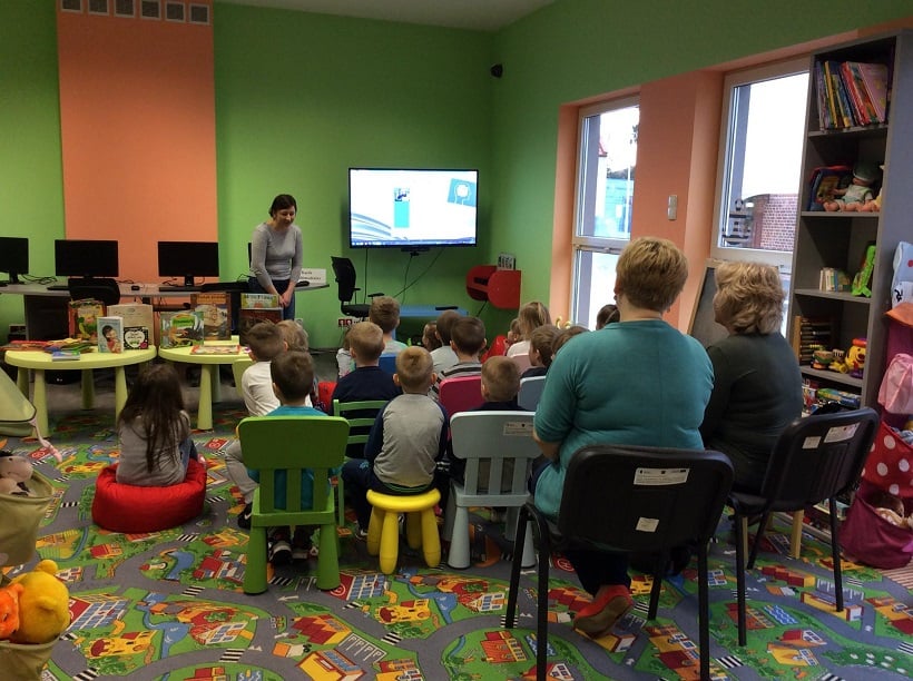 Na krzesełkach siedzą przedszkolaki, oglądają prezentację na temat powstawania książki, zajęcia prowadzi bibliotekarka Ania Wiśniewska.