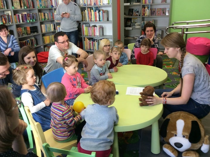 Przy stolikach siedzą dzieci z Klubu Malucha. Bibliotekarka Aleksandra czyta opowiadanie  pt. "Przygoda małego pieska".