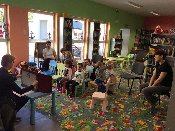 Oddział dla dzieci, grupa maluchów siedzi na krzesełkach i słucha teatrzyku Kamishibai "Brzydkie kaczątko".