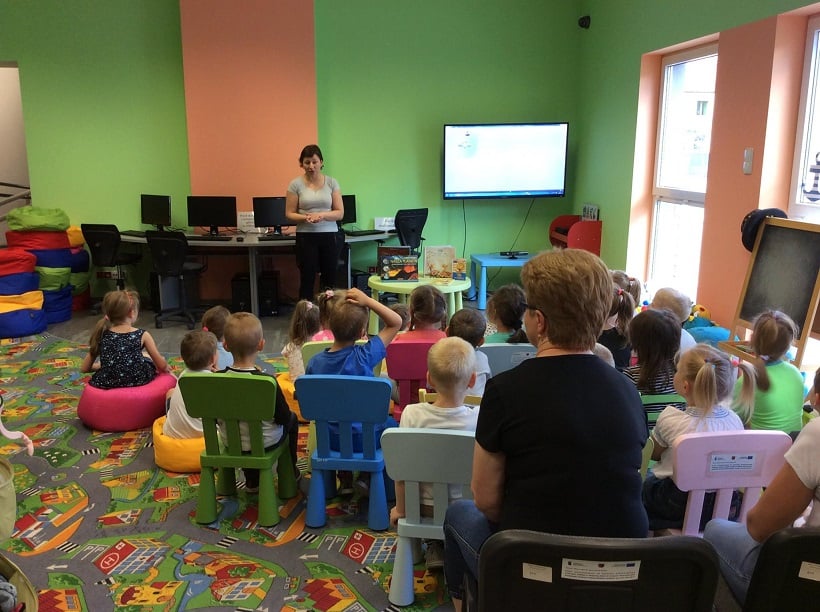 Grupa dzieci siedzi na krzesełkach i bierze udział w lekcji na temat książek,zajęcia prowadzi Ania Wiśniewska.