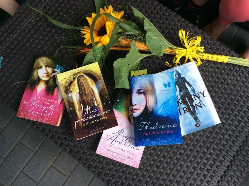Na stoliku leży kwiat słonecznik oraz pięć książek autorki Aprilynne Pike.