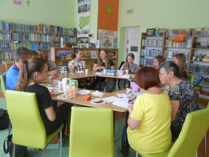 Przy stolikach siedzą uczestnicy DKK GIM NR 2 wspólnie omawiają książkę "Moją Młyńską" E. Zakrzewskiej.