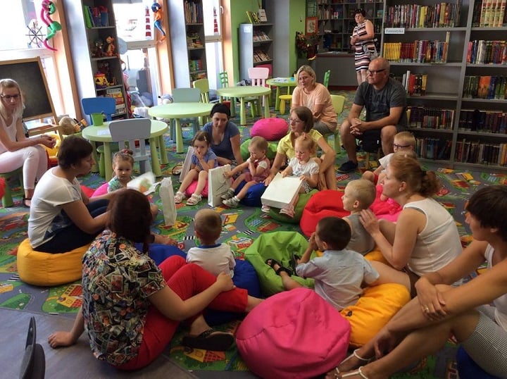 Wnętrze biblioteki. Na kolorowych pufach siedzą dzieci z upominkami z okazji zakończenia Klubu Malucha.