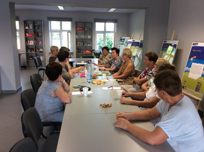 Wnętrze biblioteki,mediateka. Przy stolikach siedzą uczestnicy DKK UTW wspólnie omawiają książkę "Sekretny język kwiatów" Vanessy Diffenbaugh. 