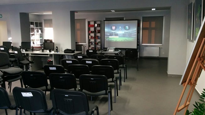 Wnętrze biblioteki,mediateka. Czarne krzesełka i projekcja gry FIFA 15 przygotowana na turniej gry komputerowej.