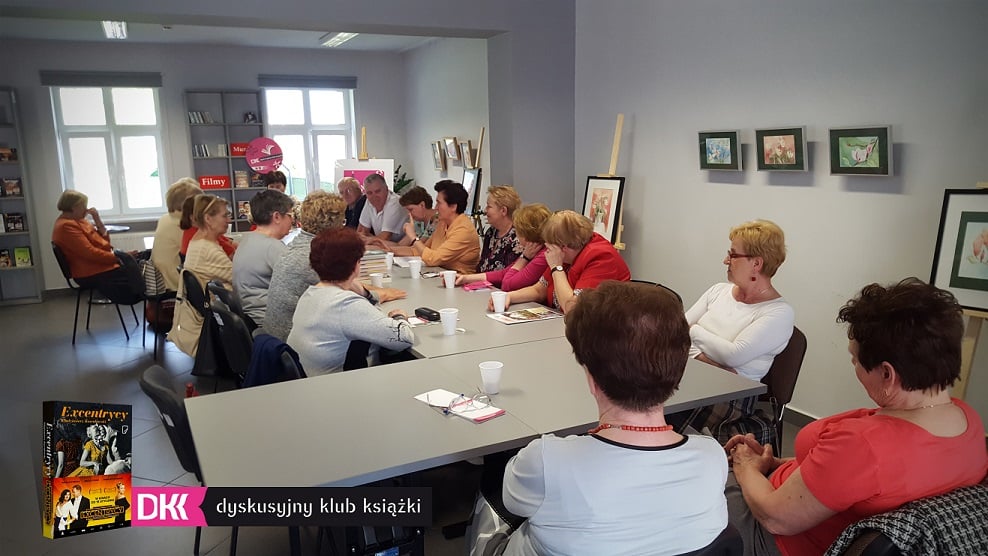 Wnętrze biblioteki,mediateka. Przy stolikach siedzą uczestnicy DKK UTW wspólnie omawiają książkę W. Kowalewskiego "Excentrycy".