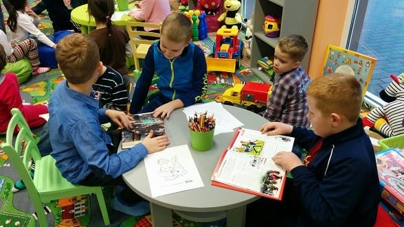 Przy stoliku siedzi czterech chłopców, dwóch chłopców czyta książki a pozostali kolorują kolorowanki. 