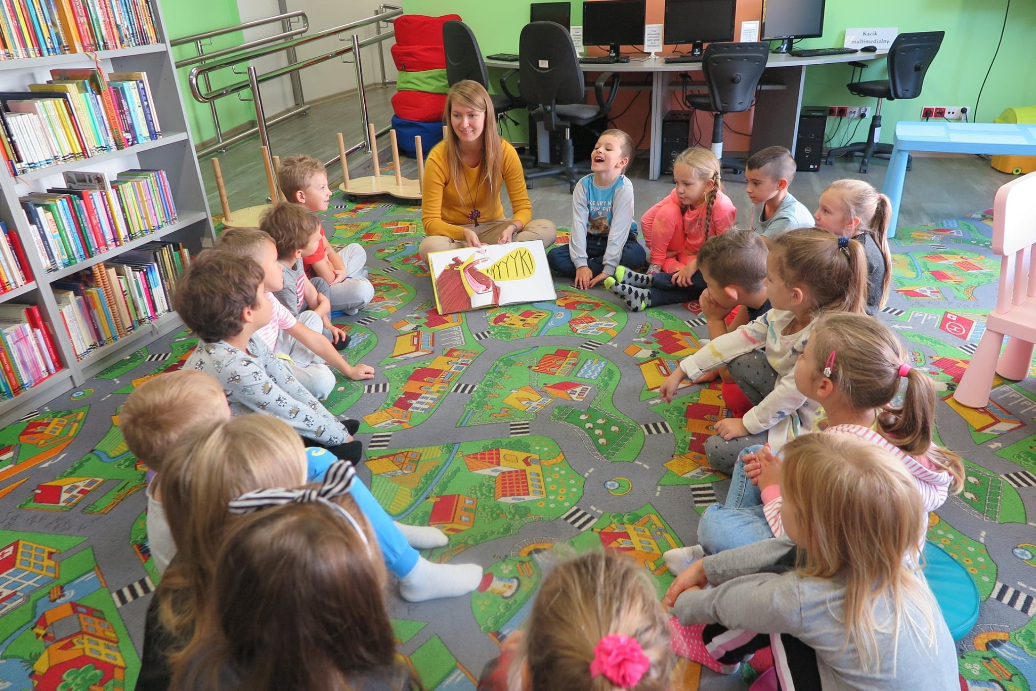 Wnętrze biblioteki, oddział dla dzieci. Przedszkolaki z grupy ''Kłapouszki'' siedzą w kole i słuchają książki ''Mysz, która chciała być lwem''. Zajęcia prowadzi Aleksandra Cybulska.