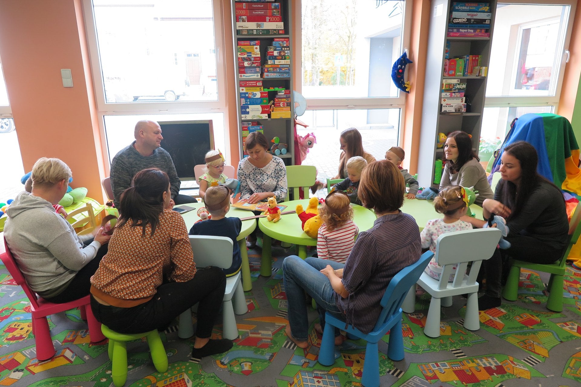 Oddział dla dzieci (Klub Malucha) przy stolikach siedzą dzieci wraz z opiekunami. Z okazji święta ''Ogólnopolskie Urodziny Książkowego Misia'',dzieci słuchają opowiadania o Kubusiu Puchatku. Zajęcia prowadzi bibliotekarka Ania Wiśniewska. 