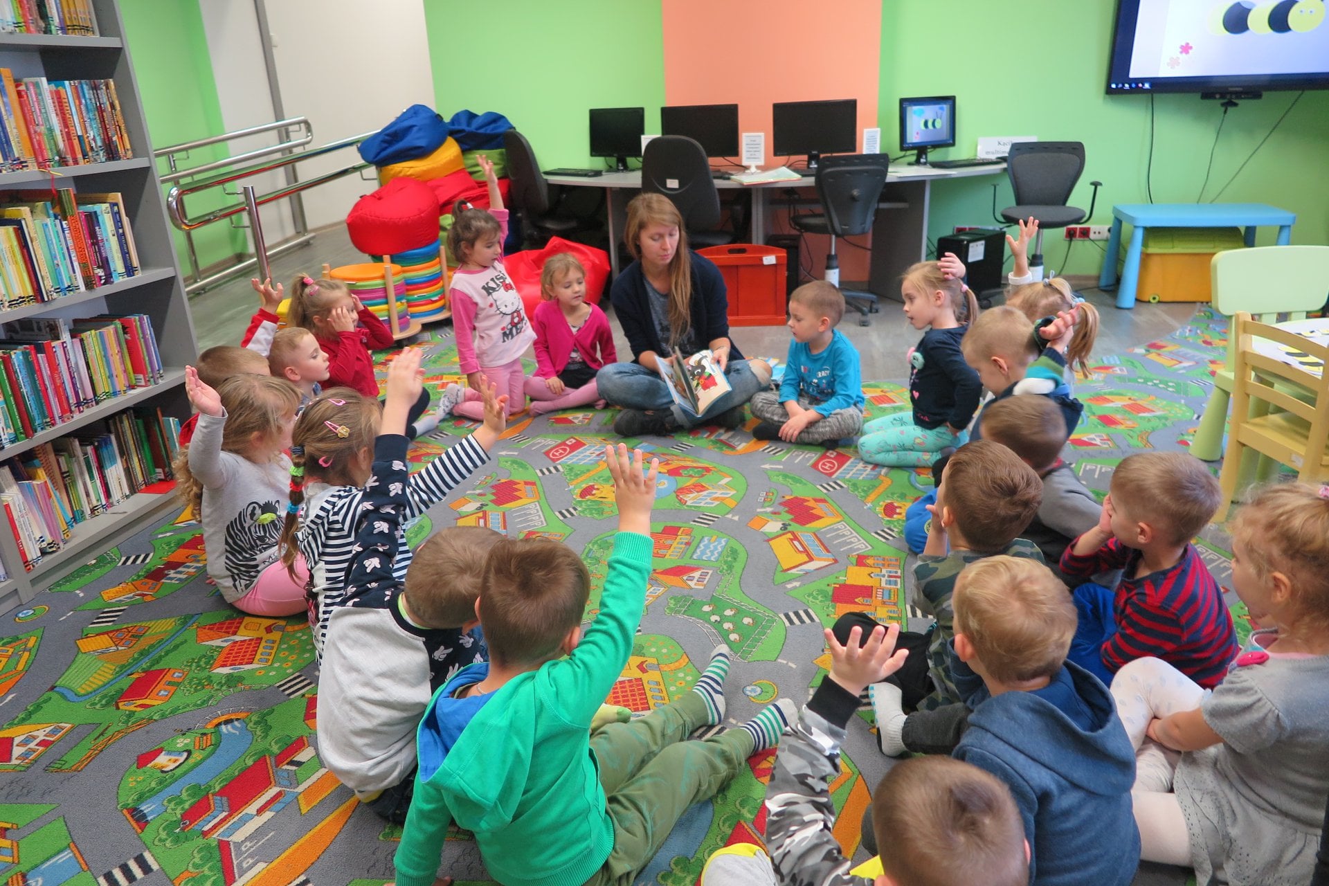 Wnętrze biblioteki. Dzieci z przedszkola nr 3 siedzą w okręgu.Zajęcia prowadzi bibliotekarka Aleksandra Cybulska. 