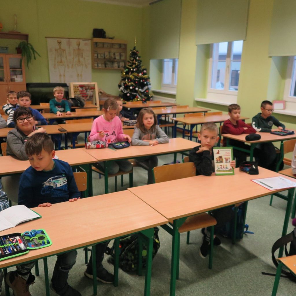 Wnętrze klasy. Dzieci siedzą w ławkach. Spotkanie DKK w Szkole Podstawowej nr 1. Z tej okazji dzieci omawiają książkę ''Piątka z Zakątka'' Krystyny Drzewieckiej. 