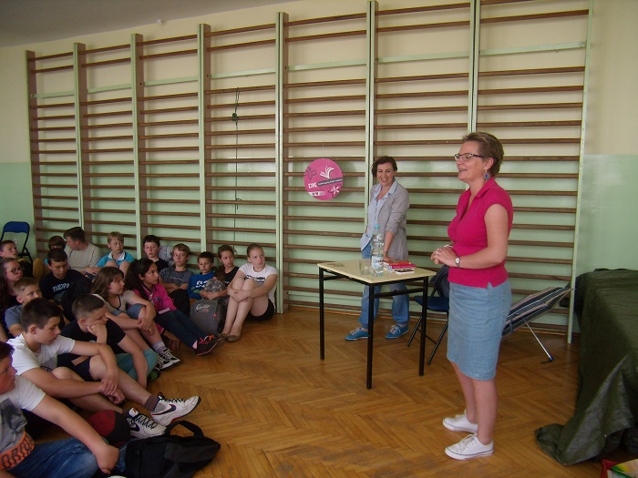 Wnętrze sali gimnastycznej, grupa dzieci bierze udział w spotkaniu z pisarką Joanną Fabicką.