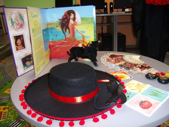 Na stoliku leży czarny kapelusz, wachlarz , czarny byk, i książka Carmen, wszystkie elementy dotyczące Hiszpanii.