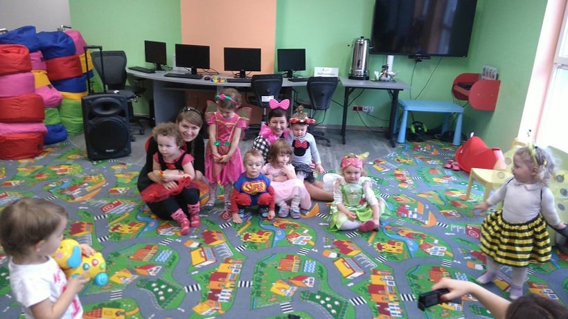 Na kolorowej wykładzinie grupa dzieci w przebraniu z bibliotekarkami Anią i Aleksandrą. 