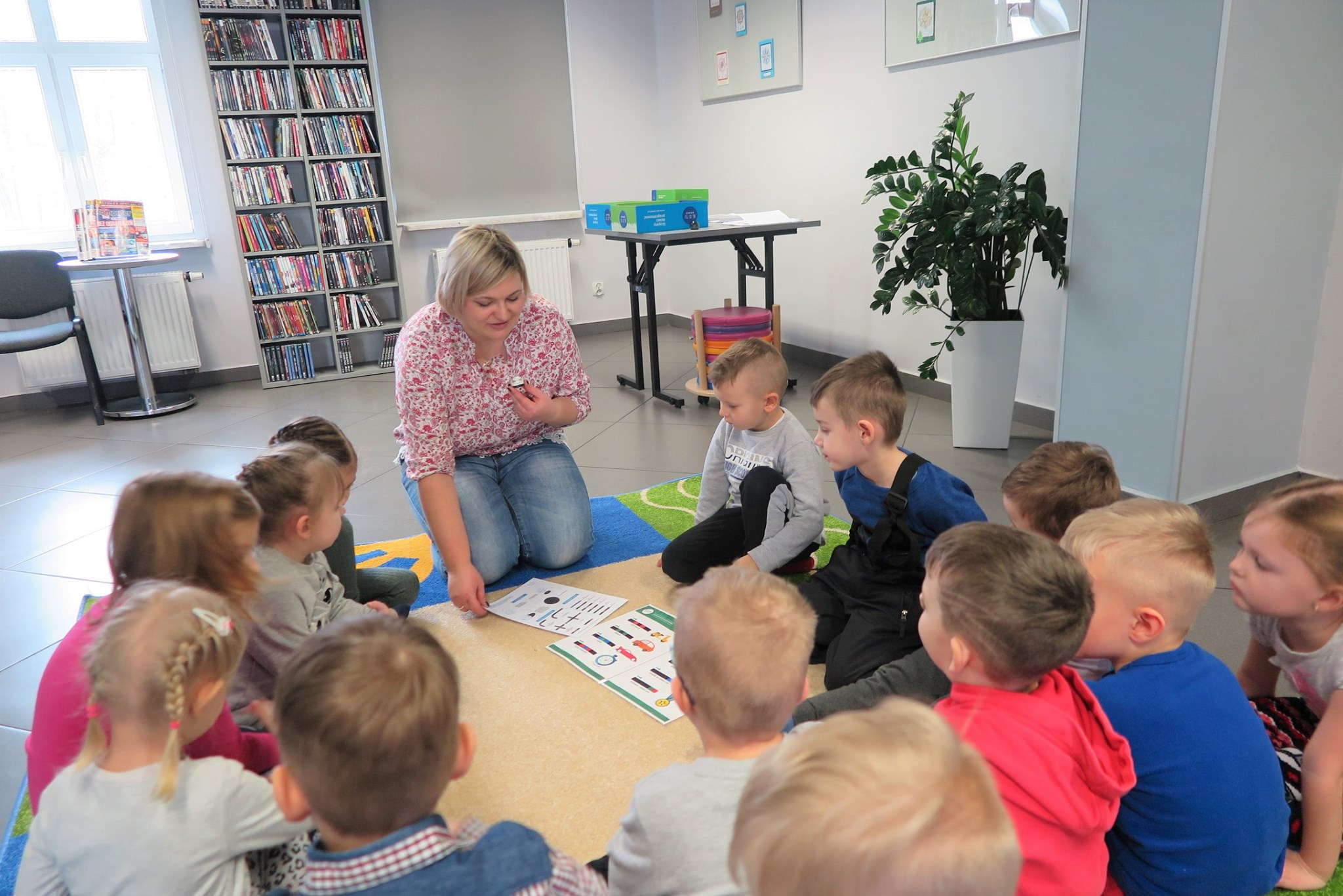 Wnętrze biblioteki mediateka. Bibliotekarka Dorota Kusik prowadzi warsztaty z programowania ozobotów dla dzieci z przedszkola nr 5 grupa ''Truskaweczki''.
