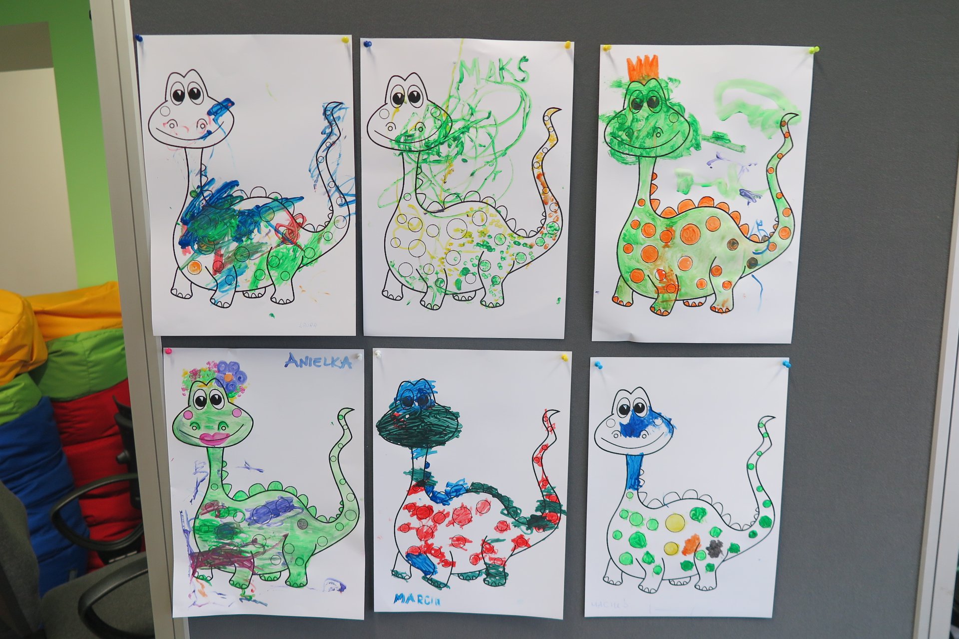 Na banerze wisi 6 kartek z postaciami dinozaurów pokolorowane przez dzieci. 