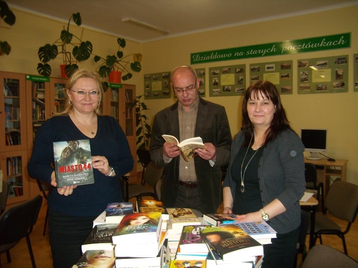 Na stoliku leżą książki podarowane od MBP dla GIM NR 1 obok stoi dyrektor MBP Justyna Lytvyn i dwóch pracowników szkoły.