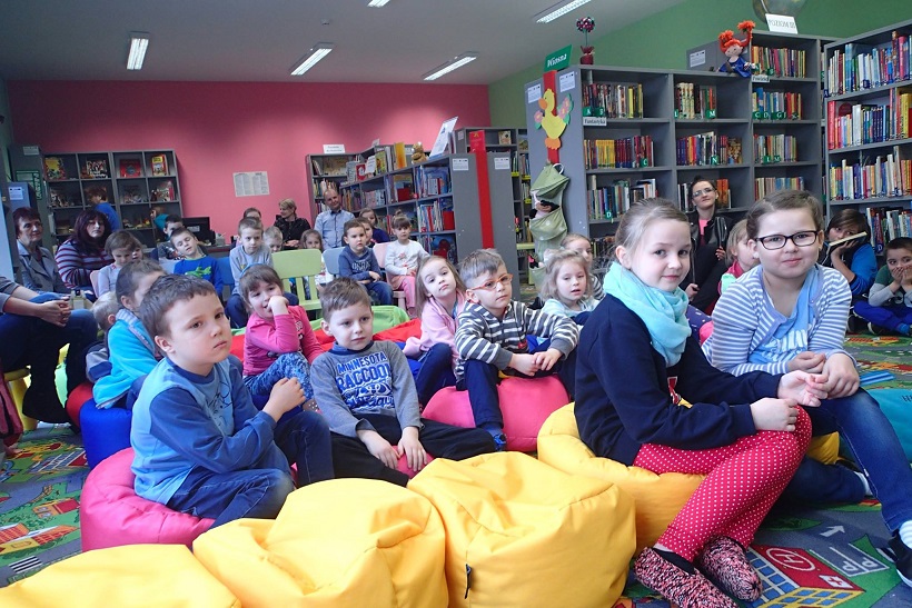 Grupa dzieci siedzi na kolorowych pufach biorą udział w spotkaniu z pisarką Wiolettą Piasecką.