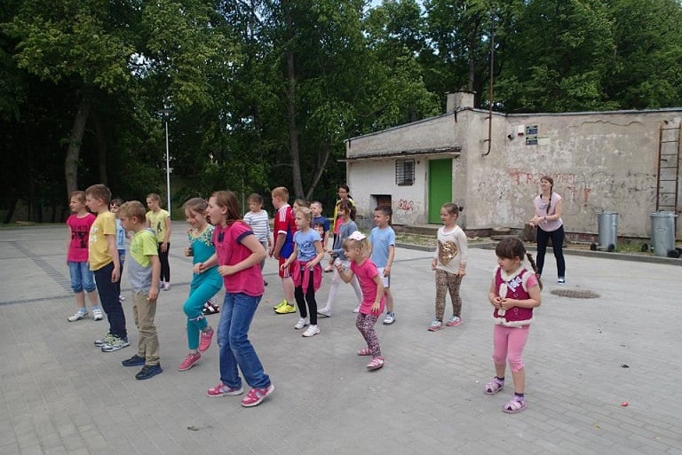 Na placu grupa dzieci bawiąca się w zbijaka.