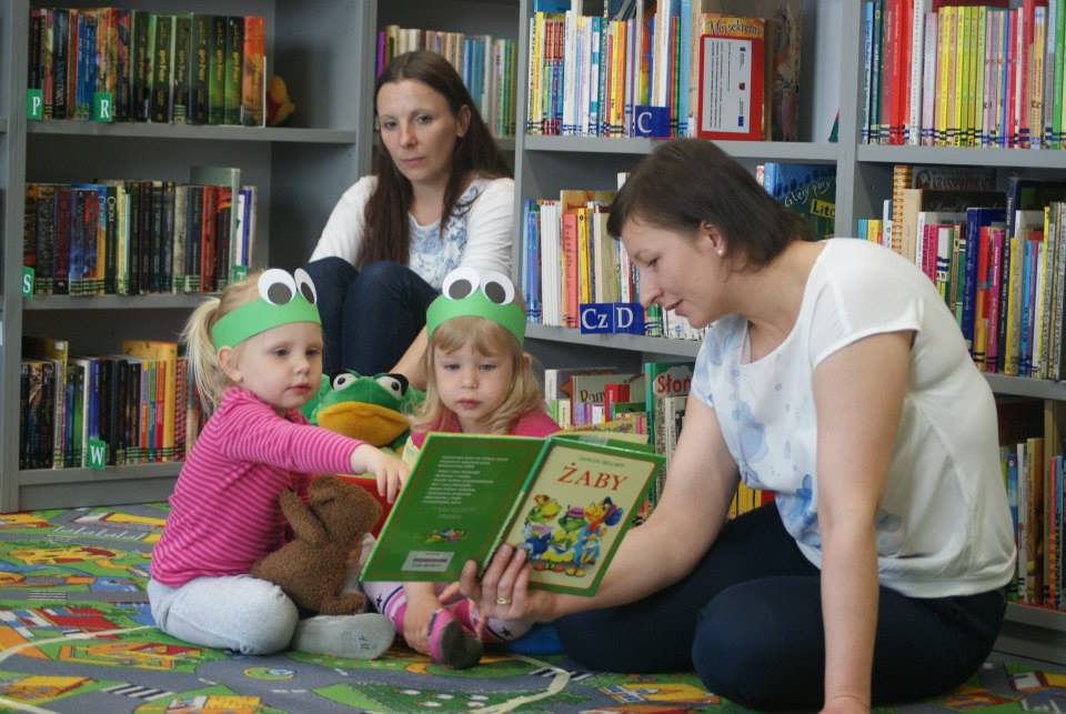 Przy regale z książkami bibliotekarka Ania Wiśniewska czyta dzieciom  opowiadania z książki „Żabki i żabki czyli słowne pułapki”.