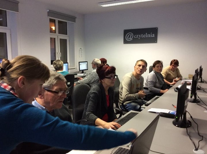 Przy komputerach siedzą uczestnicy kursu komputerowego, który prowadzi bibliotekarka Małgorzata Trąmpczyńska.