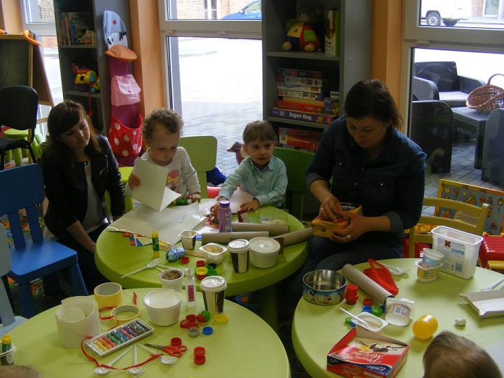 Przy stoliku siedzi dwoje dzieci z opiekunką oraz bibliotekarką Anią razem wykonują instrumenty z wcześniej zgromadzonych pojemników po artykułach spożywczych.