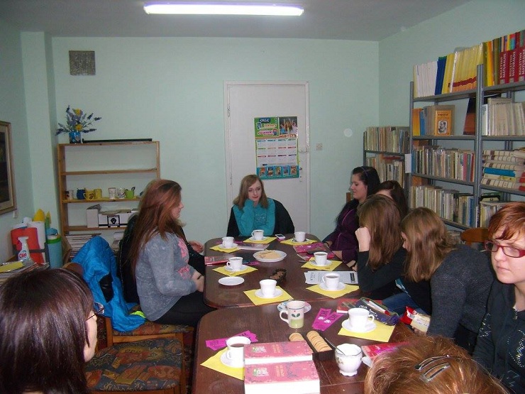 Wnętrze biblioteki, przy stolikach siedzą członkinie DKK ZS Malinowo wspólnie omawiają książkę J. Frey "W ślepym zaułku wolności. Dzieci ulicy". Na stoliku mały poczęstunek i kawa.