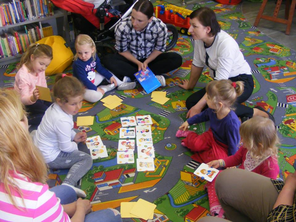 Grupa dzieci z opiekunką i bibliotekarką Anią grają w karty .