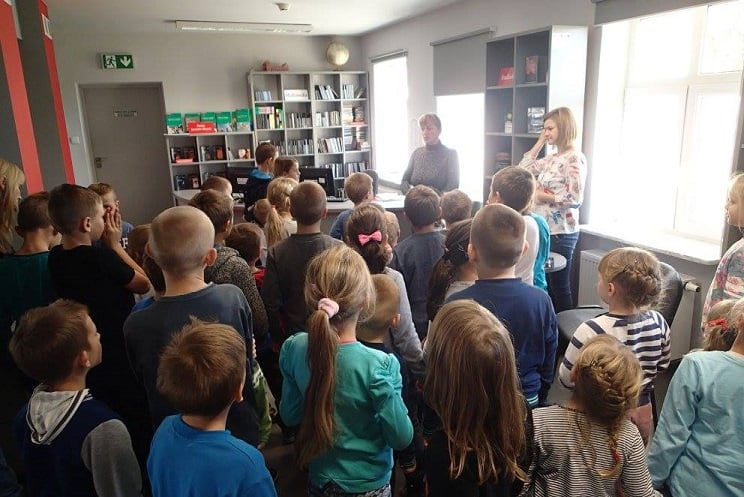 Wnętrze biblioteki. Grupa uczniów ze szkoły w Klęczkowie zwiedza oddział mediateka.