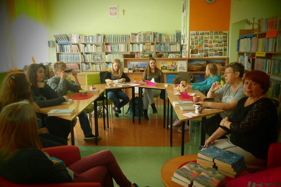 Wnętrze biblioteki szkolnej przy stolikach uczestnicy DKK GIM Nr 2 wspólnie omawiają Ruta Sepetys "Szare śniegi Syberii".