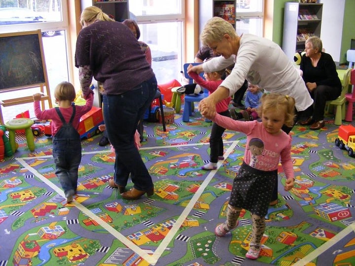 Grupa dzieci z opiekunami bawi się z figurami geometrycznymi.