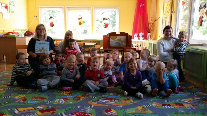 Na kolorowej wykładzinie siedzą dzieci z nauczycielkami i bibliotekarką Anią.
