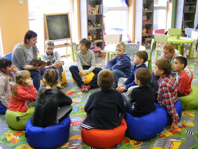 Na pufach siedzą dzieci, uważnie słuchają jak czyta bibliotekarka Ania opowiadania  pt. „Franklin mały bałaganiarz”.