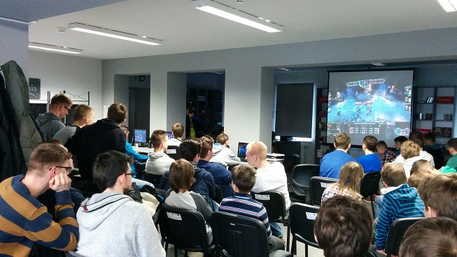 Uczestnicy i publiczność zgromadzona na turniej gier komputerowych, w tle wyświetlona prezentacja gry League of Legends.