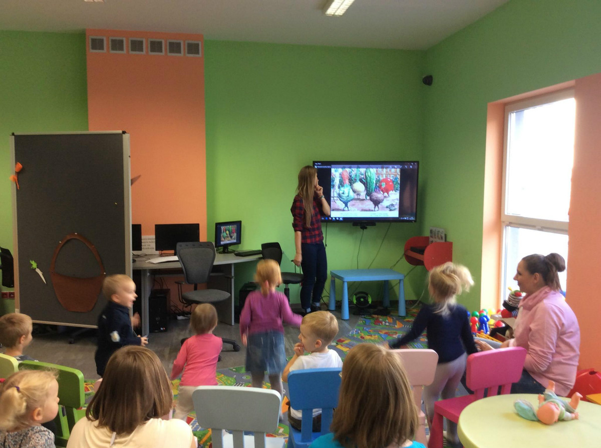 Wnętrze biblioteki, bibliotekarka Aleksandra Cybulska pokazuje dzieciom prezentację o warzywach. c