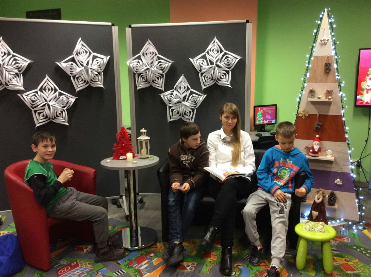 Wnętrze biblioteki. Na kanapie trzech chłopców i bibliotekarka Aleksandra Cybulska czyta opowiadania związane z Bożym Narodzeniem.