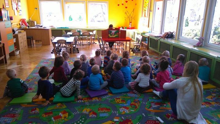 Wnętrze Przedszkola nr 4, grupa dzieci siedzi na pufach i słucha teatrzyku Kamishibai "Trzy świnki" , przedstawia bibliotekarka Ania Wiśniewska.