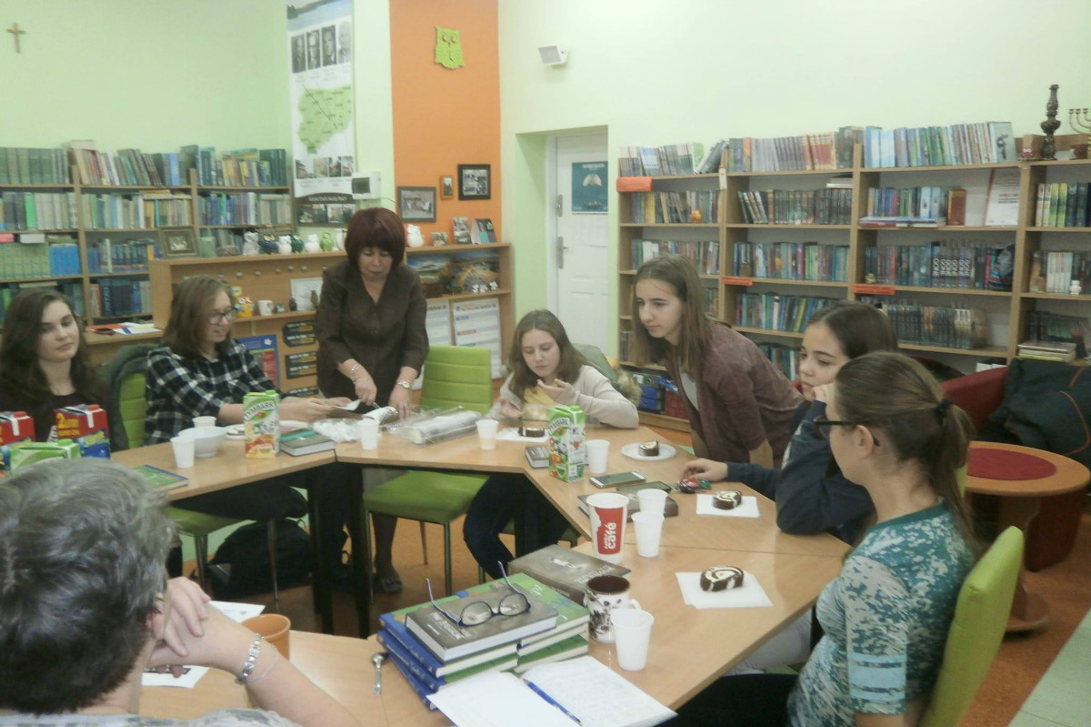 Wnętrze biblioteki. Grupa młodzieży z DKK GIM NR 2 wspólnie omawia książkę "Osobliwy dom pani Peregrine" . 