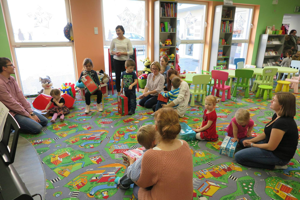 Wnętrze biblioteki. Grupa dzieci z opiekunami bawi się podczas zajęć w Klubie Malucha. 
