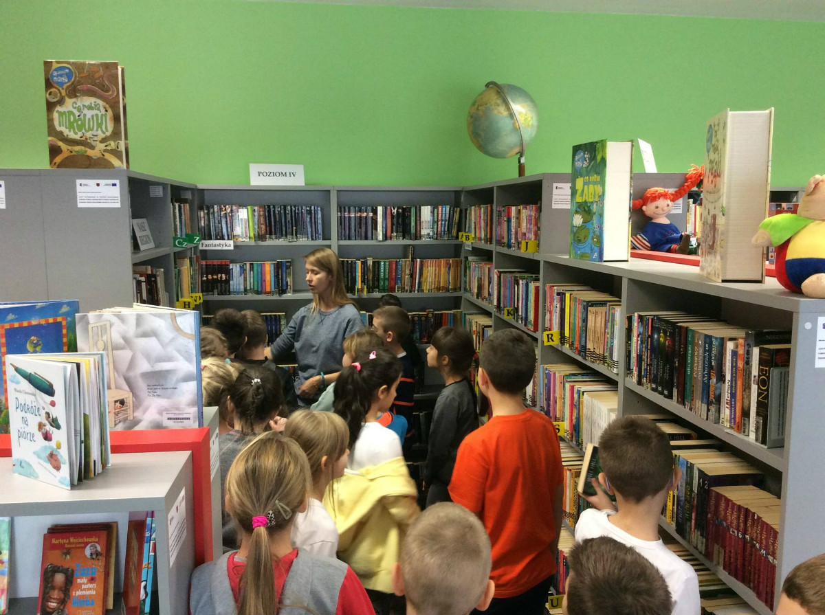 Wnętrze biblioteki. Uczniowie ze SP NR 3 zwiedzają oddział dla dzieci, bibliotekarka Aleksandra Cybulska pokazuje dzieciom książki.