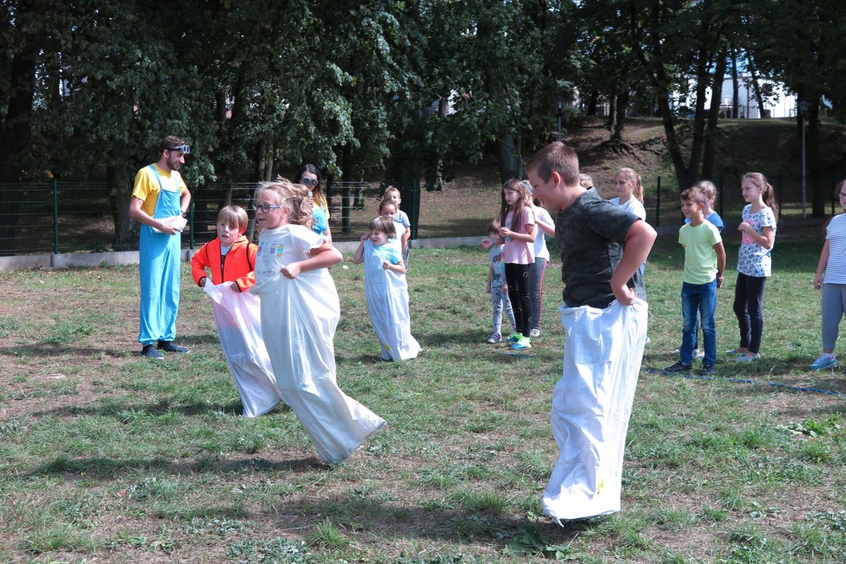 Na placu obok MBP w Działdowie dzieci biorą udział w zabawie w wyścigu skaczą w workach.