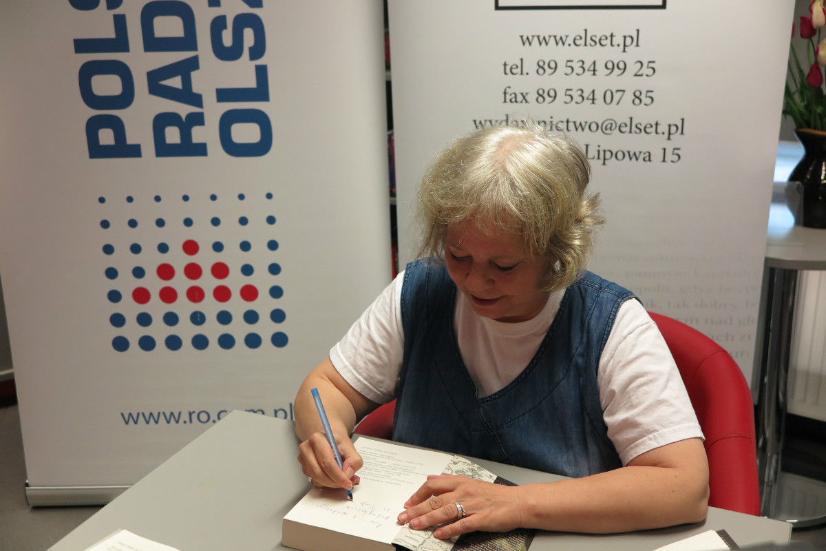 Przy stoliku Pani Joanna Żamejć podpisuje swoją książkę czytelnikom.