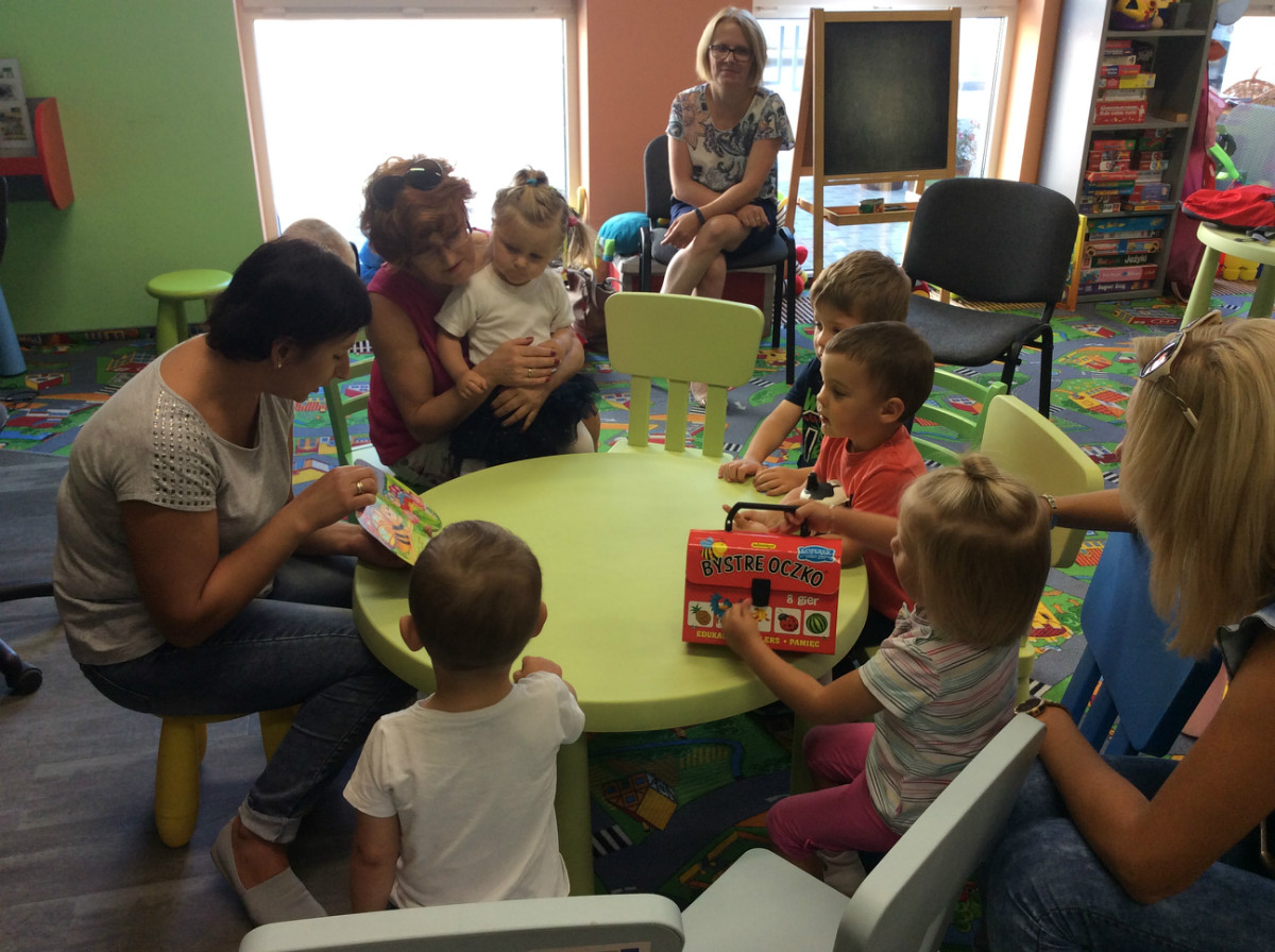 Przy stoliku z bibliotekarką Anią Wiśniewską siedzą dzieci z opiekunkami, słuchają bajki o motylku Kamilku.