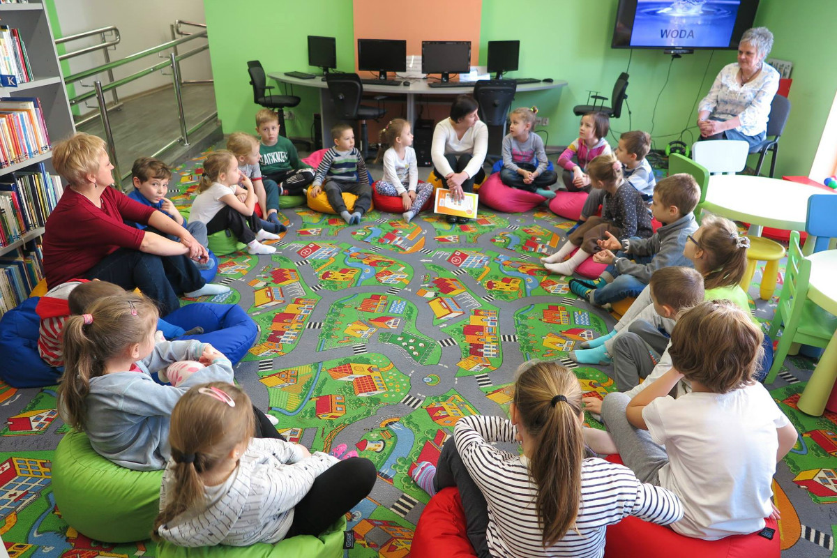 Wnętrze biblioteki. W kole siedzą dzieci z Przedszkola nr 3, biorą udział w zajęciach o ekologii, jak dbać o środowisko.
