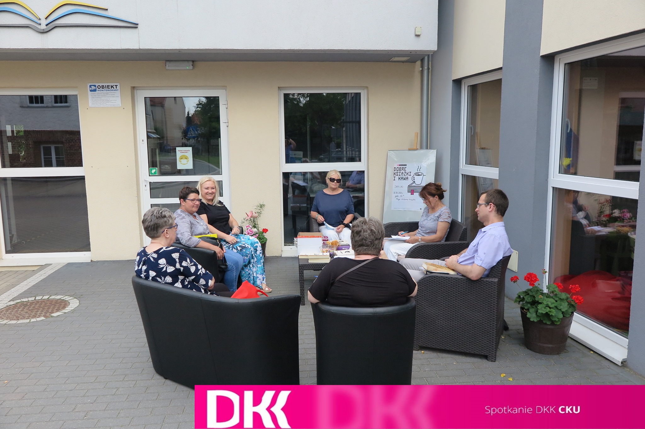 Przed biblioteką w Działdowie pani dyrektor Justyna Lytvyn rozmawia wraz z goścmi klubu DKK przy CKU. W miłej atmosferze rozmawiają o swoich ulubionych książkach. 