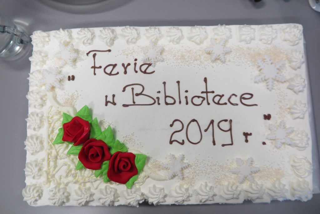 Biały tort z napisem ''Ferie z Bibliotece 2019r''.