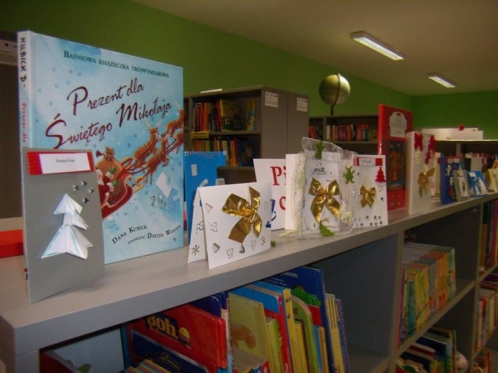 Na regale z książkami stoją kartki świąteczne oraz książka pt.,, Prezent dla Świętego Mikołaja''.