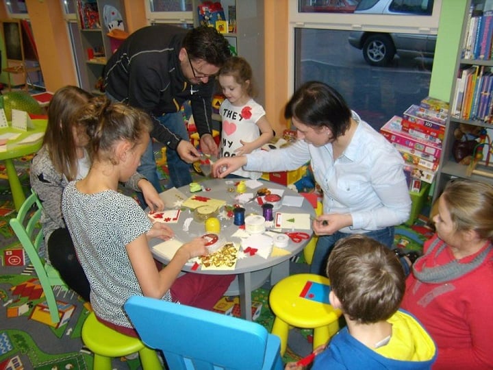 Przy stoliku siedzi grupa dzieci i dwie bibliotekarki wspólnie wykonują kartki świąteczne.
